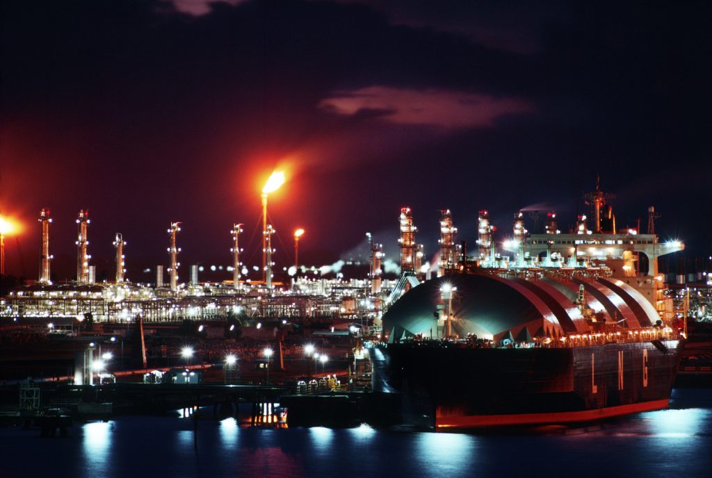 Liquid Natural Gas tanker at port with LNG liquefaction plant in background.